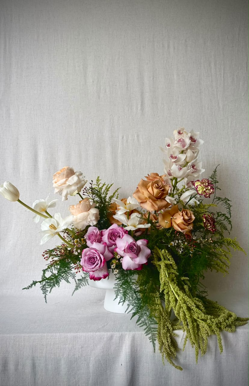 A hand holds a peach, copper and ivory bouquet with trailing amaranthus against warm afternoon linen