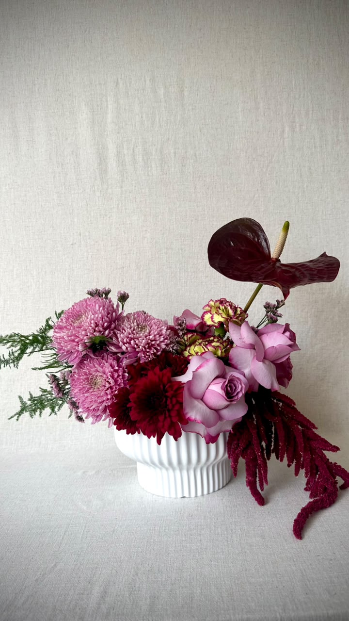 Jewel-toned arrangement of burgundy chrysanthemum, mauve roses and a deep red anthurium in a fluted vase